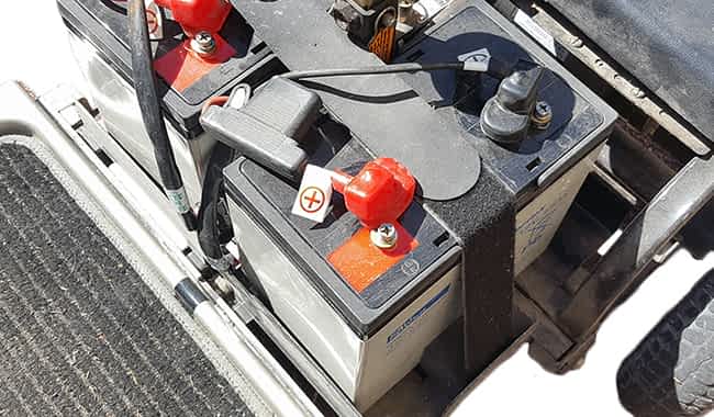 Batterie GEL 60 Ah de MK dans un scooter handicapé avec le faisceau de câbles déconnecté et une clef plate dévissant le boulon de la borne de la batterie